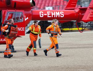Air ambulance crew in orange flight suits walking away from a red helicopter during an emergency response