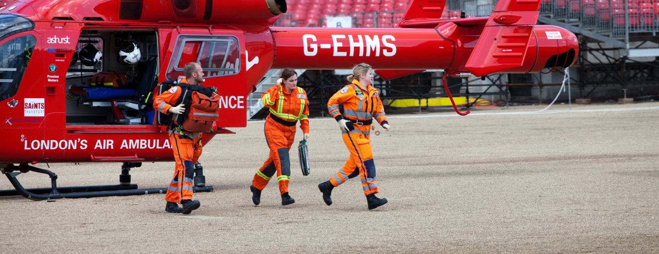 Air ambulance crew in orange flight suits walking away from a red helicopter during an emergency response