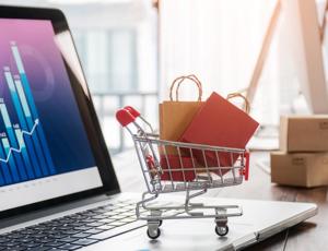 Small shopping trolley graphic filled with packages placed on a laptop displaying data charts