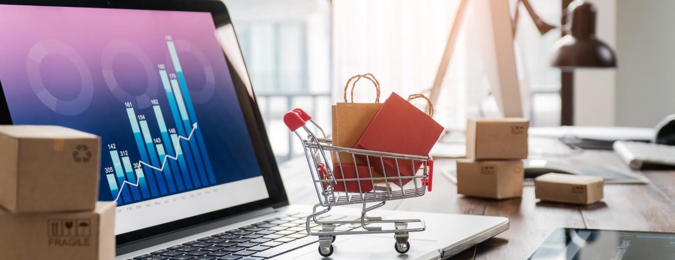 Small shopping trolley graphic filled with packages placed on a laptop displaying data charts